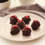 Schokoladen-Eier mit roten Beeren auf einem weißen Teller, ideal für vegane Osterleckereien.