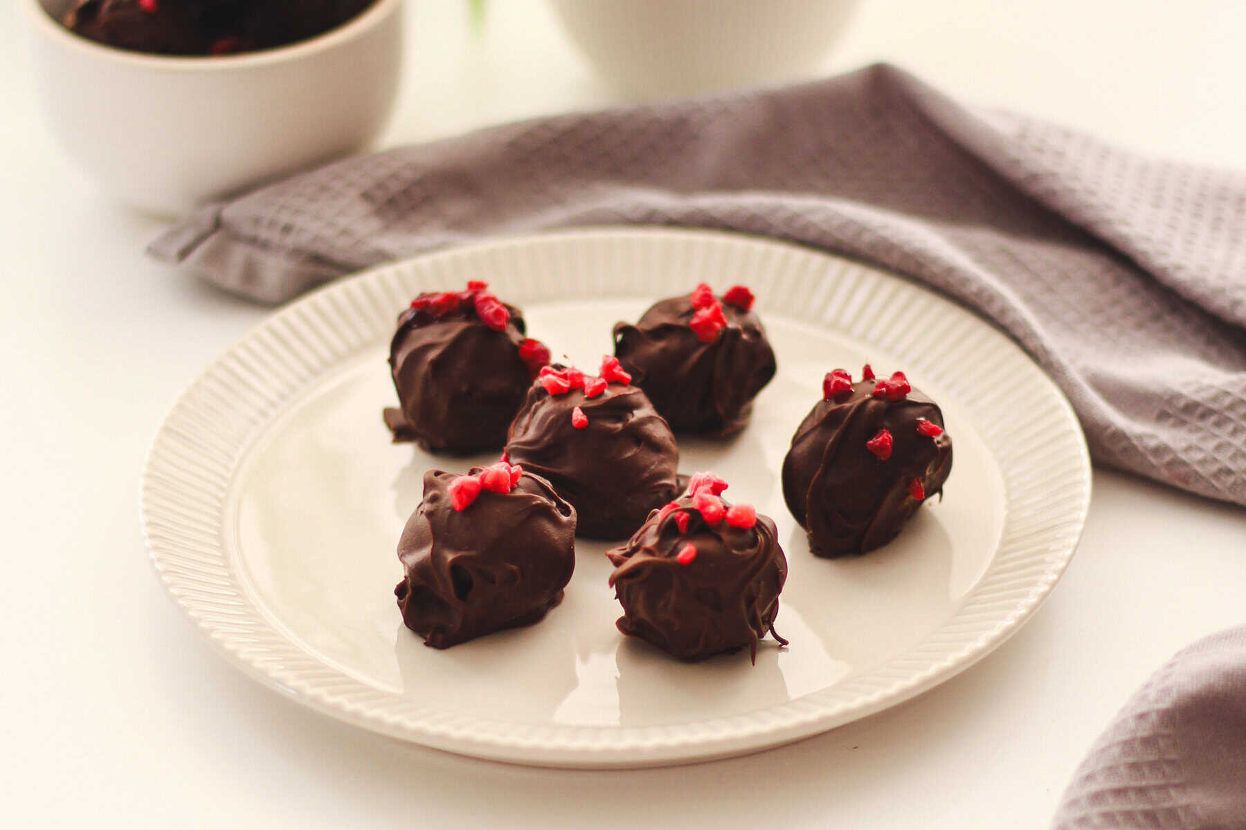 Schokoladen-Eier mit roten Beeren auf einem weißen Teller, ideal für vegane Osterleckereien.